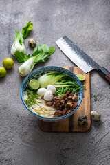 Japanese ramen soup with chicken, egg, chives and bok choy on concrete background.