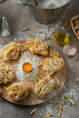 Freshly made tagliatelle pasta with eggs and flour on wooden board