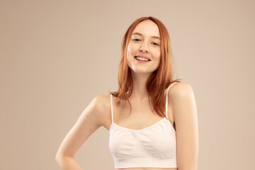 Obraz premium Portrait of young beautiful red-haired girl posing with tender smile isolated over grey studio background. Self-love