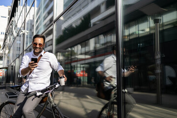 Business man sitting on bike and holding cell phone and cup of coffe