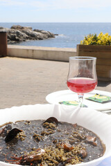 Black rice with cray fish plate and wine glass with sangria on a table by the ocean