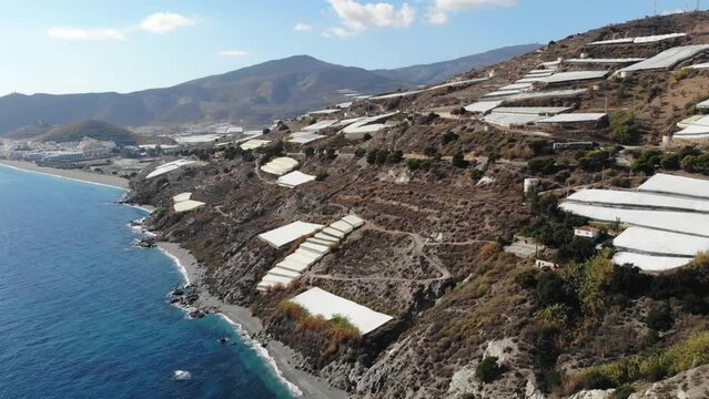 Drone Aerial View Of A Large Group Of Greenhouses On A Hillside By The Sea