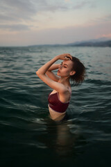 Slim gorgeous woman in a purple swimsuit is posing in the water.