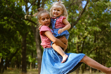 Obraz na płótnie Canvas Cute sisters happy together celebrating Children's Day June 1 outdoors. Kids activities in summer camp. Kids have fun in park forest. Little girls on nature. Older sister holding baby girl in her arms