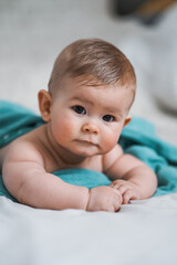 cute little naked 6 month old baby lying on stomach and looking up in prone position after bathing wrapped in turquoise towel at home