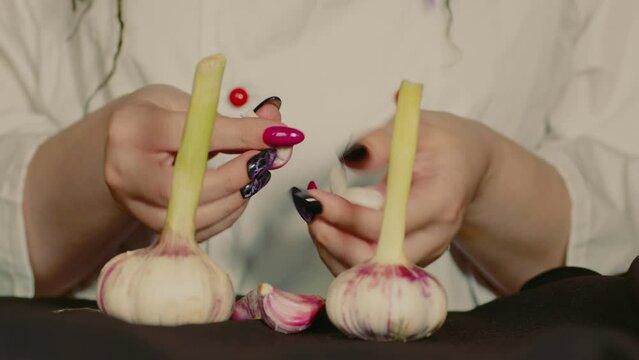 Close-up, an unrecognizable girl cook is peeling young garlic. Woman peels fresh garlic from the skin on the kitchen table