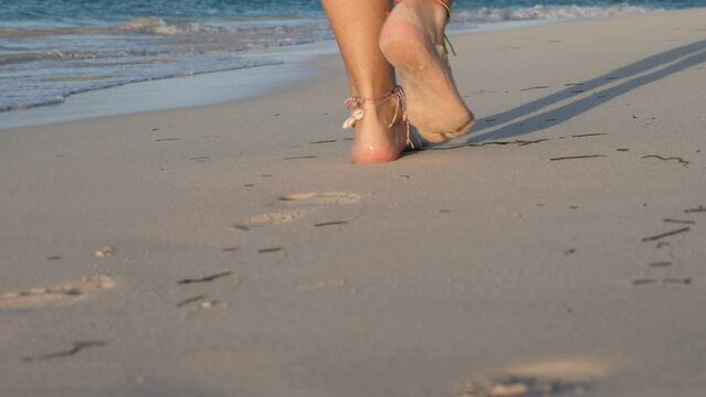 Woman legs, walking along sandy beach. Leaving footprints on sand