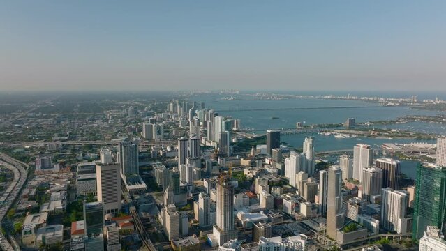 Breath taking aerial panoramic footage of modern city borough along sea bay lit by sun at golden hour. Miami, USA