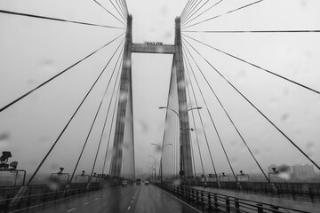 Naklejka premium Vidyasagar Setu over river Ganges, known as 2nd Hooghly Bridge in Kolkata,West Bengal, India. Abstract black and white image shot aginst glass with raindrops all over it, monsoon image of Kolkata.