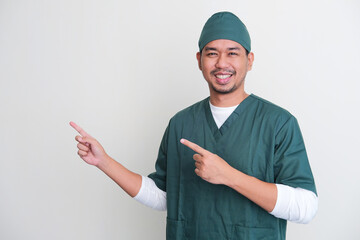 Asian hospital nurse smiling while pointing to his right - obrazy, fototapety, plakaty