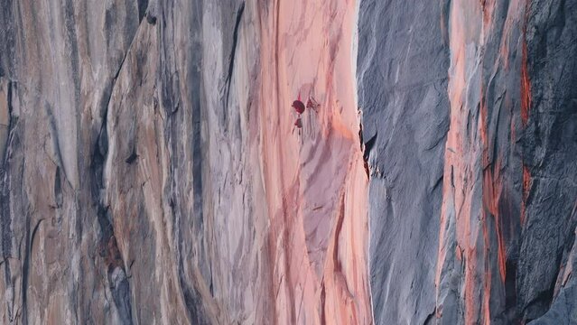 Mountain climber hanging on rope at El Capitan mountain in cinematic pink sunset reflecting from scenic sheer cliff rock. Yosemite park Firefall 6K RED camera USA. Extreme climbing climbing efforts