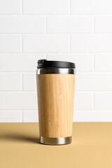 Reusable thermos cup for drinks on a beige kitchen table against a white brick wall. Concept of plastic-free and zero waste living. Sustainable lifestyle. Personal takeaway beverages cup
