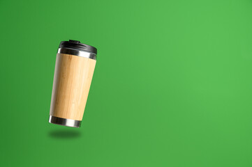 A reusable thermos cup for drinks flies in the air on a green background. Concept of plastic-free and zero waste living. Sustainable lifestyle. Personal takeaway beverages cup.