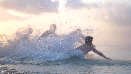 Group of happy friends at sunset running into water getting wet and making splashes swimming in the sea