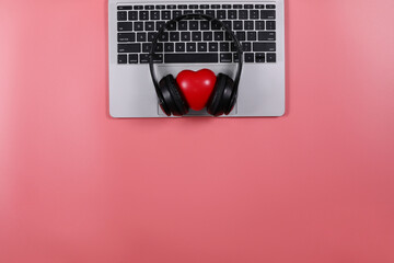 Black headphones with red heart placed on a laptop isolated on pink background. Flat Lay photography with copy space.