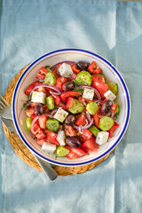 Greek salad with feta cheese, olives, tomato, cucumber and red onion, healthy vegeterian mediterranean diet food, low calories eating. Blue fabric background, top view