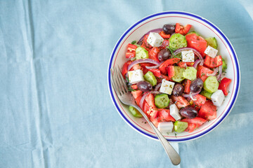 Greek salad with feta cheese, olives, tomato, cucumber and red onion, healthy vegeterian mediterranean diet food, low calories eating. Blue fabric background, top view