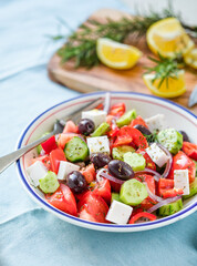 Greek salad with feta cheese, olives, tomato, cucumber and red onion, healthy vegeterian mediterranean diet food, low calories eating. Blue fabric background, top view