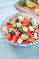 Greek salad with feta cheese, olives, tomato, cucumber and red onion, healthy vegeterian mediterranean diet food, low calories eating. Blue fabric background, top view