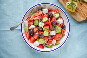 Fototapeta na wymiar Greek salad with feta cheese, olives, tomato, cucumber and red onion, healthy vegeterian mediterranean diet food, low calories eating. Blue fabric background, top view