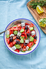 Greek salad with feta cheese, olives, tomato, cucumber and red onion, healthy vegeterian mediterranean diet food, low calories eating. Blue fabric background, top view