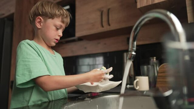 Little boy washing dishes in kitchen. Baby Dish Washing.