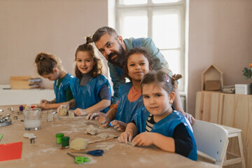 Group of little kids with teacher working with pottery clay during creative art and craft class at...