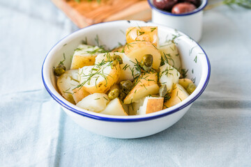 Potato salad with dill and olives in a  bowl on a blue  background.  Healthy food, vegan and lean recipes.