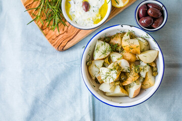Potato salad with dill and olives in a  bowl on a blue  background.  Healthy food, vegan and lean recipes.