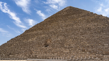 Fototapeta na wymiar The Great Pyramid of Cheops on a background of blue sky and clouds. The masonry of the walls and the opening- the entrance inside are visible. Egypt. Giza
