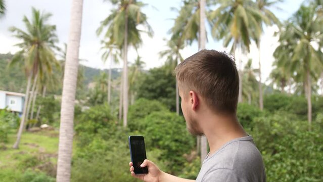 Young man with mobile phone taking photo in a jungle