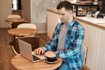 Portrait of handsome casual man 35 years old sitting on table in cafe, working online with laptop...