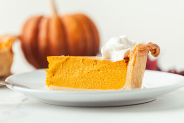 Cut slice of pumpkin pie close up on white background. Autumn orange cake