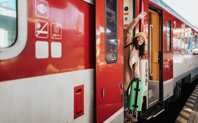 Happy young traveler woman with luggage getting in the train at train station platform