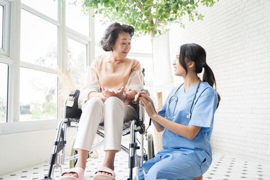 Young Asian nurse talking to a smiling senior female patient on a wheelchair and comforting her.