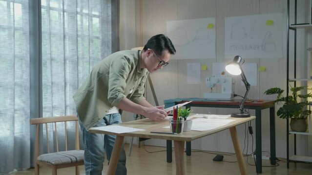 Side View Of Asian Man Designer Is Arranging The Layout Bond On The Table At The Office
