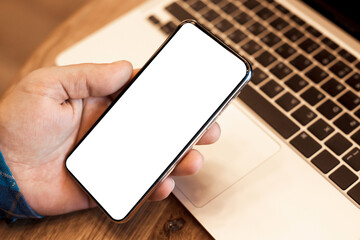 Mock up closeup photo mans hand holding smartphone with white screen for text on laptop 