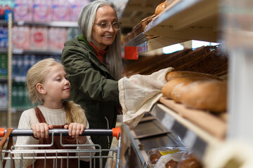Fototapeta na wymiar Grandmother with her granddaughter buying bread in supermarket.
