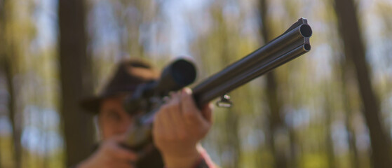 Close-up of hunter man aiming with rifle gun on prey in forest.