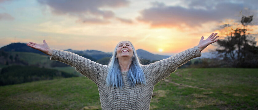 Senior Woman With Arms Outstretched And Face Up At Park On Spring Day