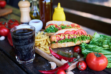 BBQ hot dog served with vegetables and French fries and sauces on wooden serving board