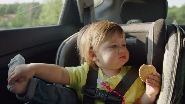 The girl rides in a high chair and plays. The child tears off socks and keeps a cookie in the car.