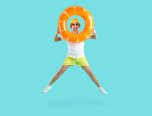 Summer. Cheerful funny man looking through inflatable circle bouncing with him light blue background. Joyful playful guy in shorts, T-shirt and panama has fun with swimming circle with orange design