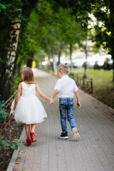Naklejka na ściany i meble Cute couple kids boy and girl hold hands on walk in summer. Girl child in high heels, kids play date