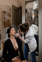 Makeup artist makes makeup for a sexy girl in a black dress with big breasts in a stylish toilet