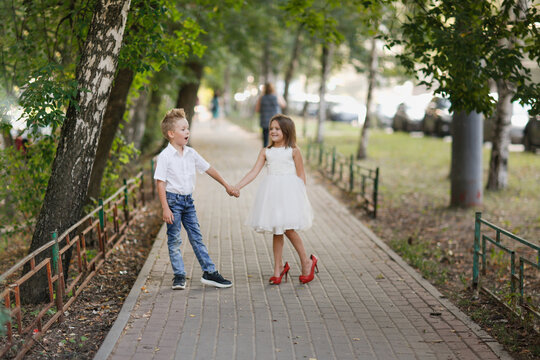 Cute Couple Kids Boy And Girl Hold Hands On Walk In Summer. Girl Child In High Heels, Kids Play Date