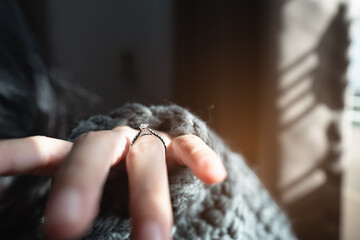 Close up of an elegant engagement diamond ring on woman finger with dark gray sweater winter clothe. love and wedding concept. Soft and selective focus.