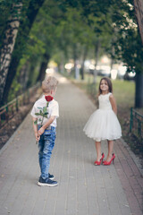 cute couple of children boy and girl, boy gives his girlfriend rose for walk in summer. Girl child in high heels, children play dating and courtship, relationship and growing up concept