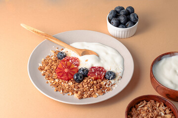breakfast table with granola bowl with greek yogurt decorated by blood oranges, blueberry and coconut. beige background. ingredient for breakfast. top view