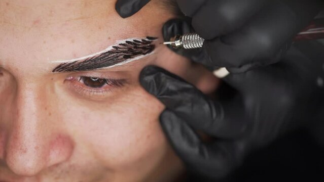 Close up shot of half male face microblading procedure to making permanent eyebrows makeup in a beauty salon